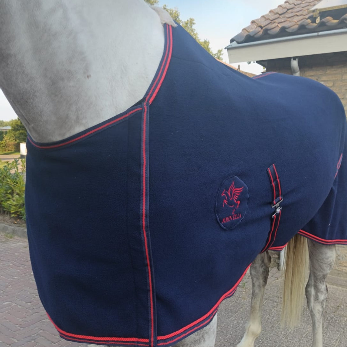 Side view of John Elia navy fleece horse rug fitted on horse, showing breast protection flap and adjustable surcingles.